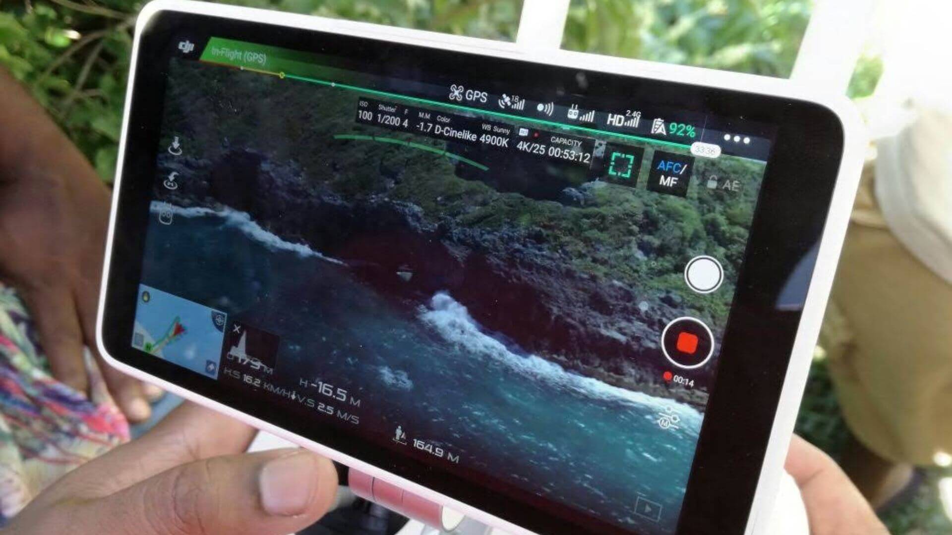 Un écran de tablette affiche une vue aérienne saisissante de la côte rocheuse de la Guadeloupe, capturée lors d'une session de tournage par une compagnie de théâtre locale pour leur projet multimédia.