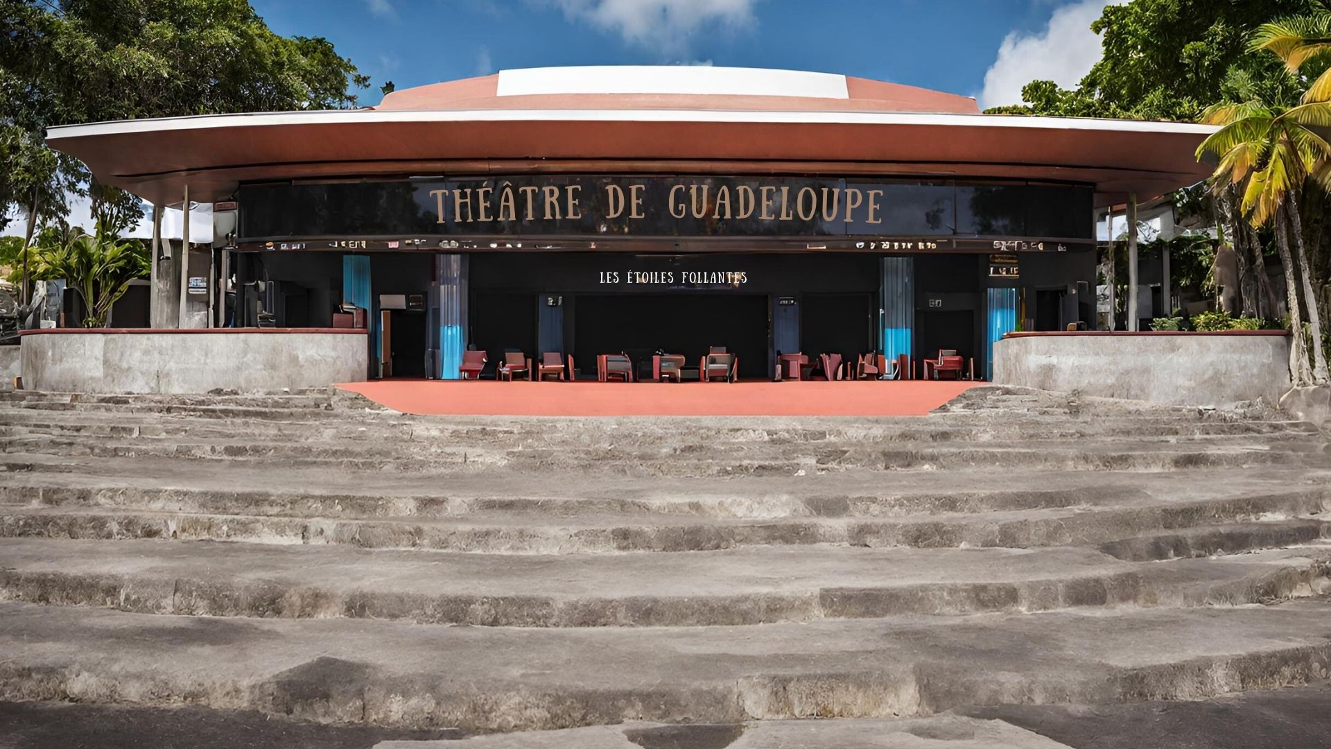 Façade extérieure du Théâtre de Guadeloupe, avec son entrée spacieuse accueillant les visiteurs sous un ciel bleu clair. Le bâtiment moderne présente une architecture arrondie, des marches en béton menant à des portes ouvertes sous un auvent, et des chaises d'attente sur le côté, prêtes à recevoir les spectateurs avant le spectacle. La végétation tropicale et le nom 'Les Étoiles Follantes' ajoutent une touche locale distinctive